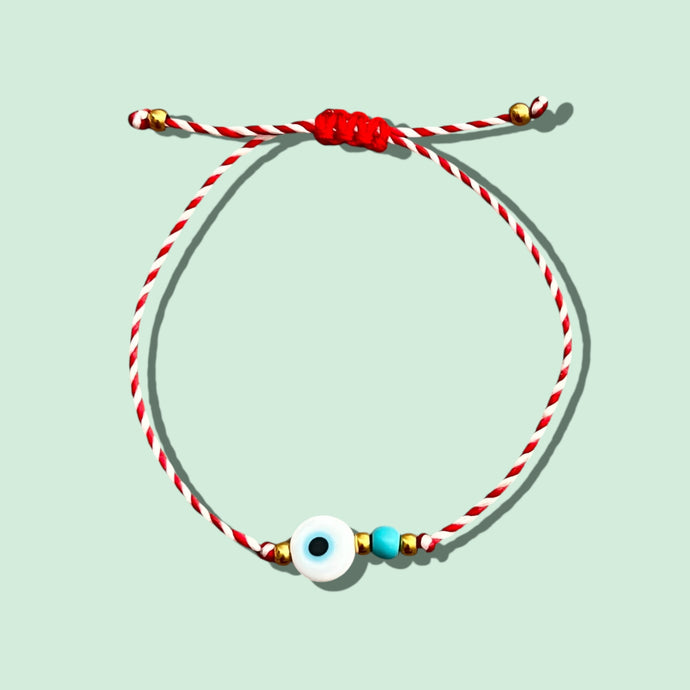 Close-up of a red and white waxed cord bracelet with white evil eye and turquoise bead.