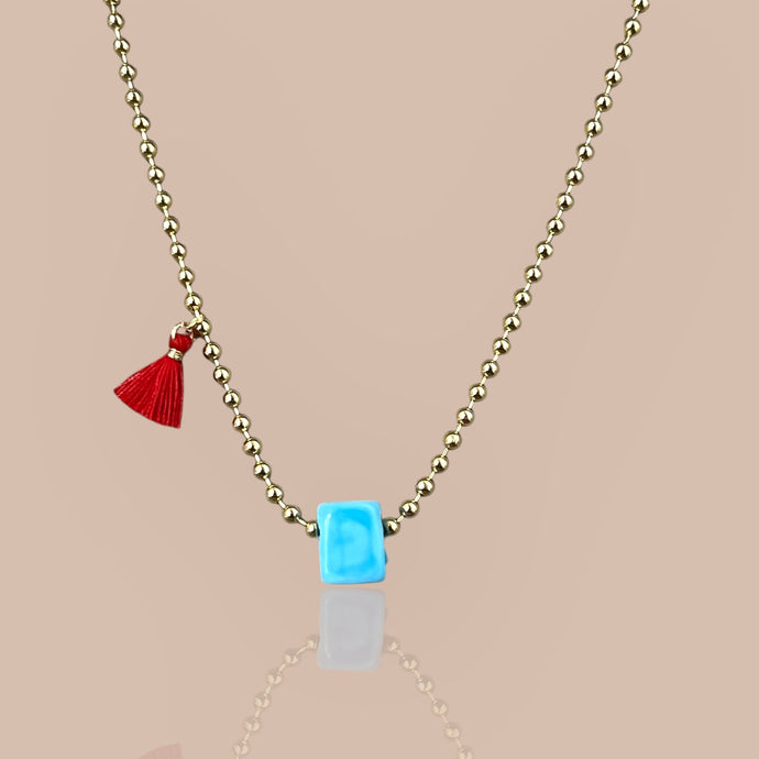 Close-up of a gold beaded chain necklace with a turquoise cube pendant, symbolizing luck and elegance