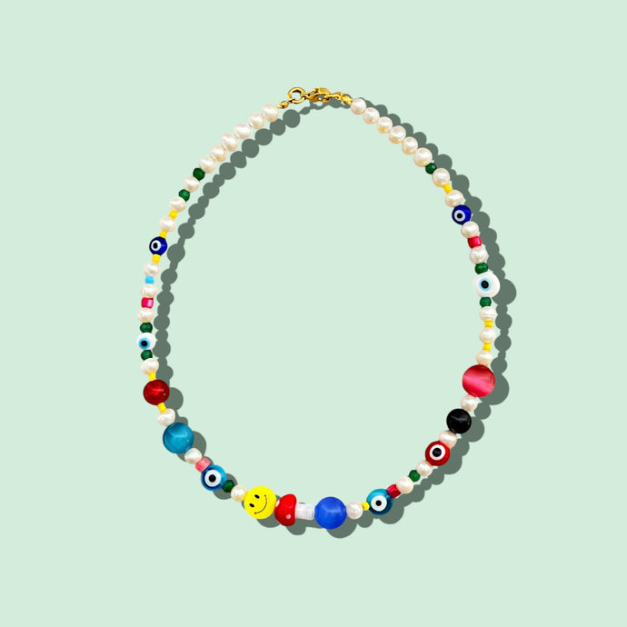 Close-up of a freshwater pearl choker necklace with smiley face, mushroom, evil eye, and semi-precious gemstones.