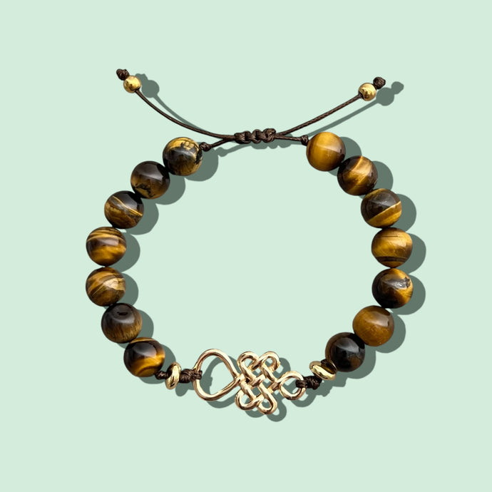 Close-up of a tiger’s eye bracelet with an endless knot charm, adjustable sliding closure.